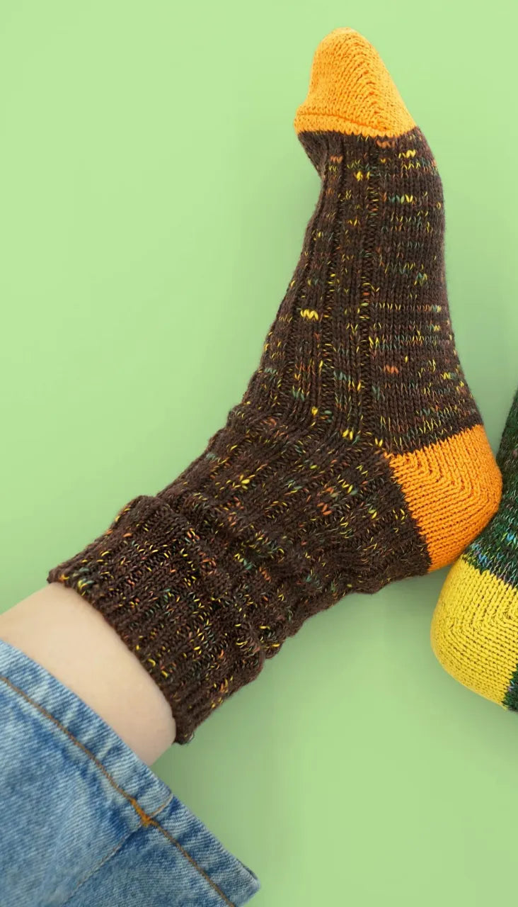 Pair of feet wearing brown and green socks with yellow accents on a green background