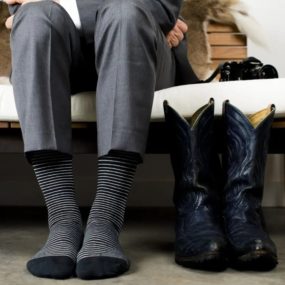 Person wearing gray pants and black and white striped compression socks with a pair of black cowboy boots on a wooden floor.