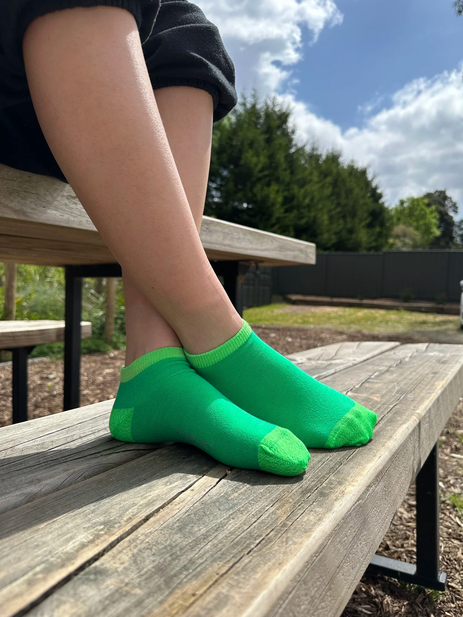 Person wearing green socks sitting on a wooden bench outdoors