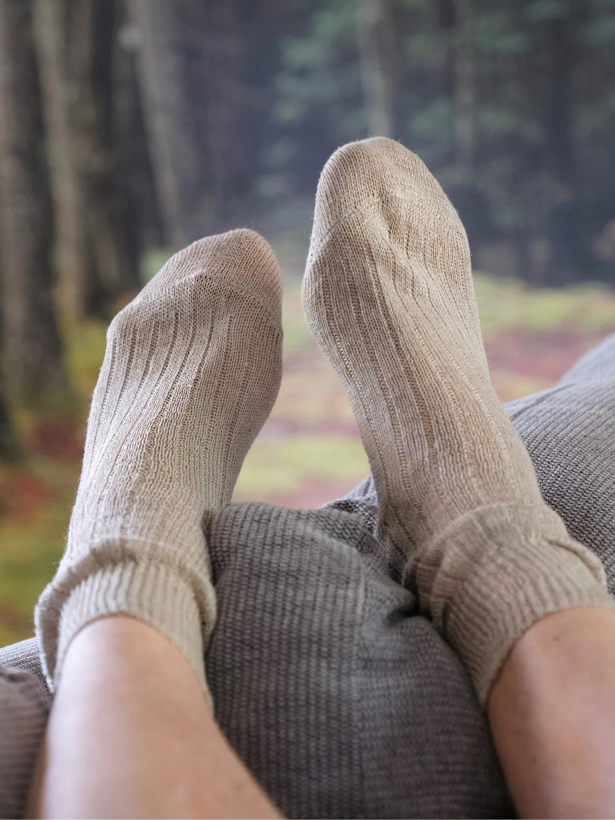 Beige socks worn by a person sitting in a chair with a blurred forest background