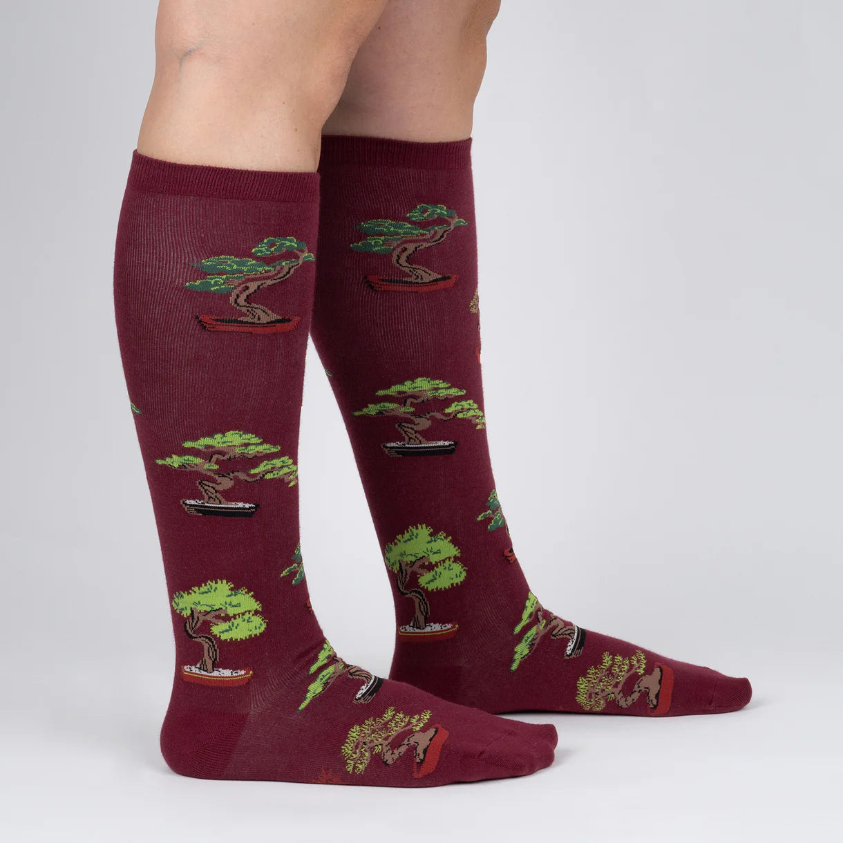 Maroon knee-high socks with bonsai tree pattern worn by a person on a light gray background