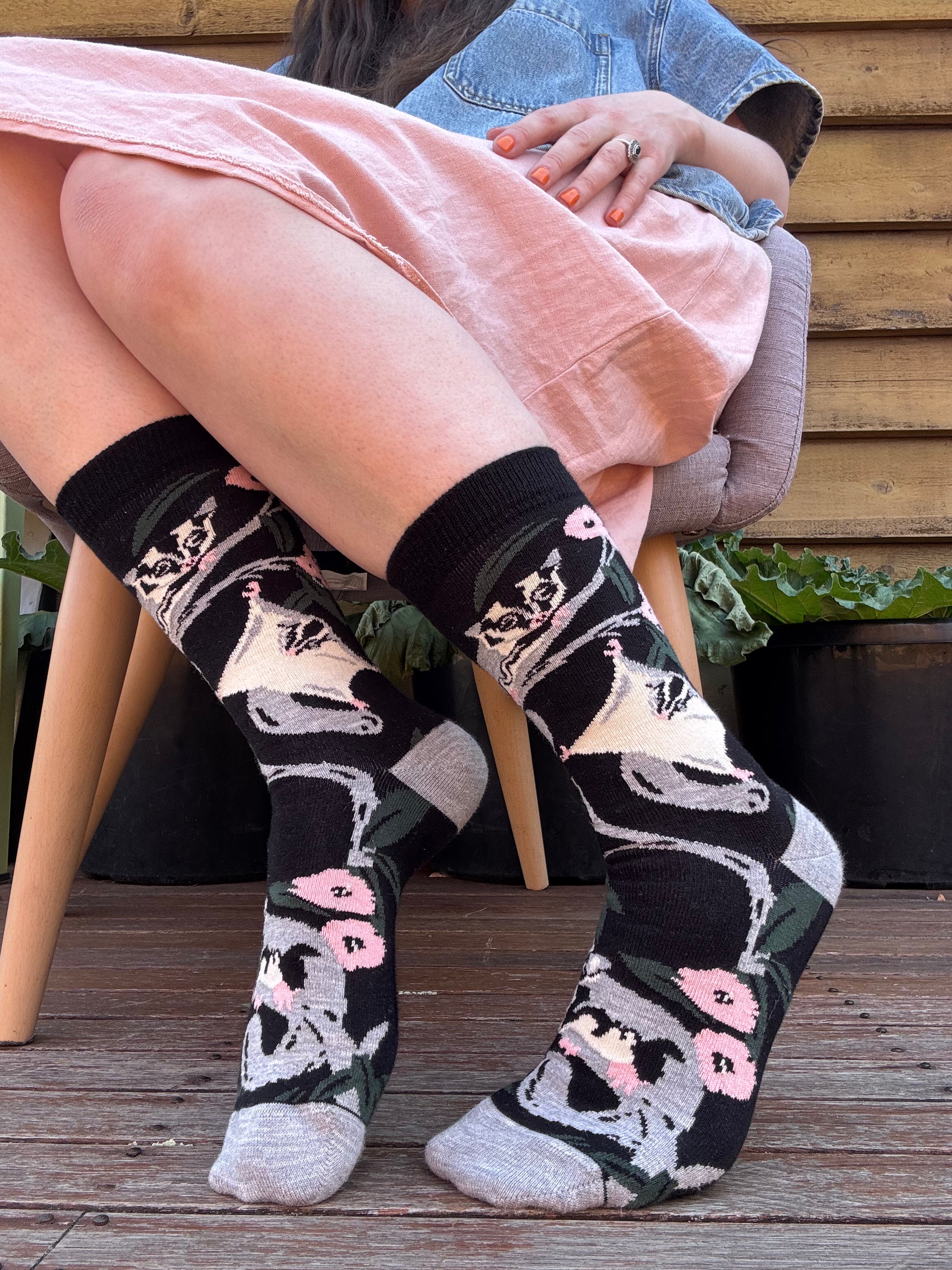 Person wearing black socks with sugar glider and flower patterns on a wooden deck.