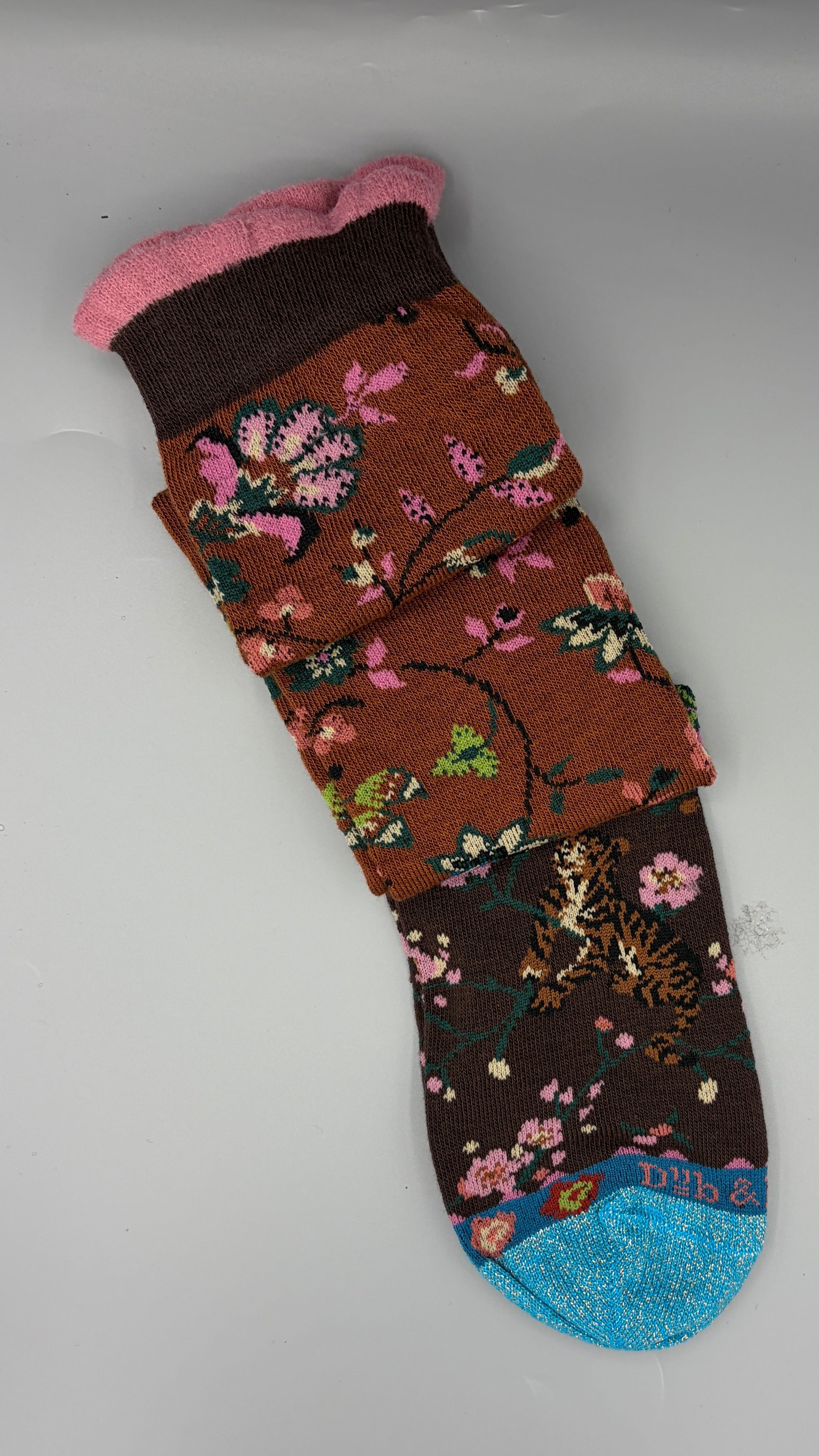 A single knee-high sock with a brown floral pattern, blue toe, and pink cuff, resting on a light gray surface.