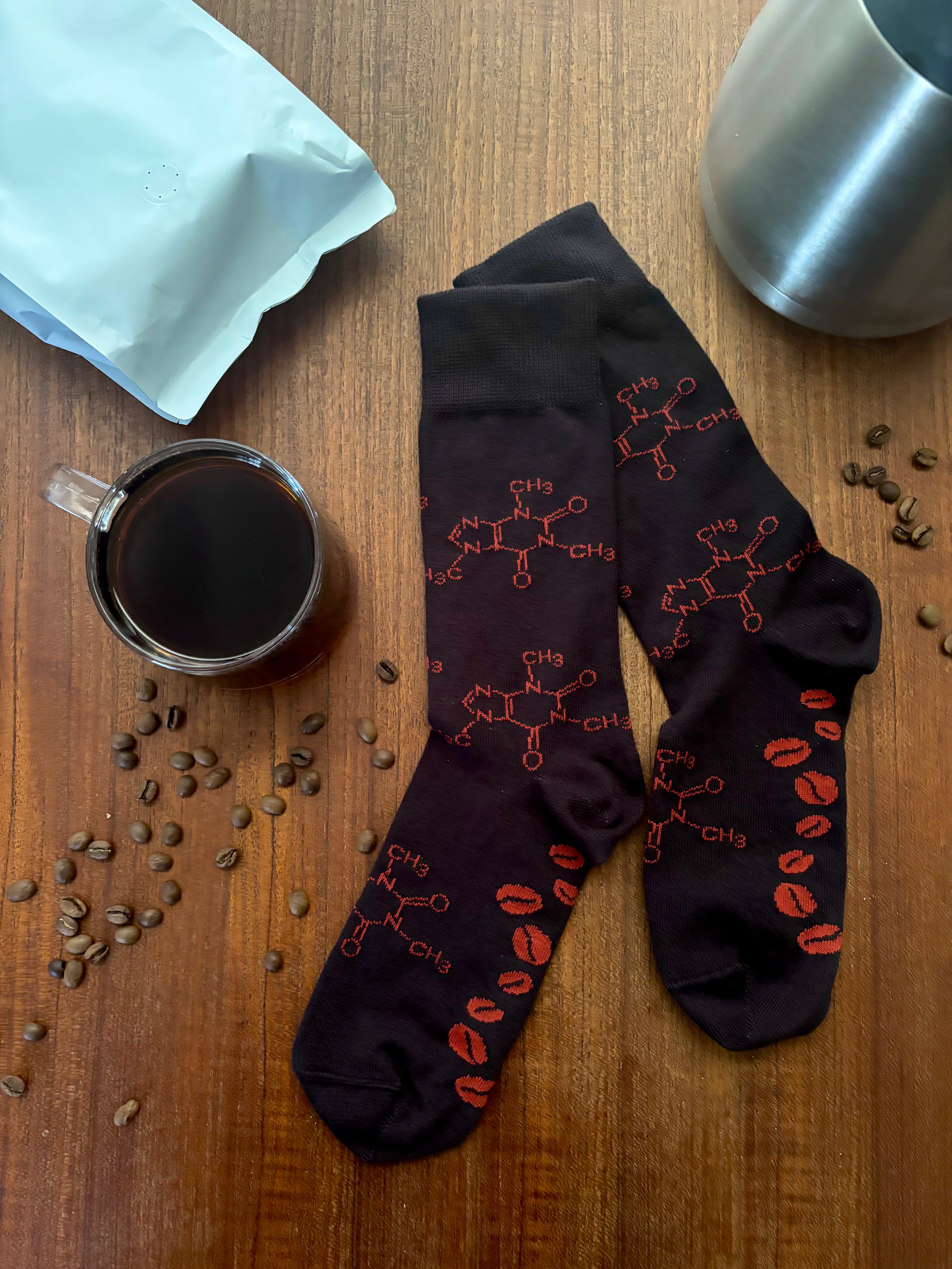 Black socks with red designs on a wooden surface with coffee cups and beans.