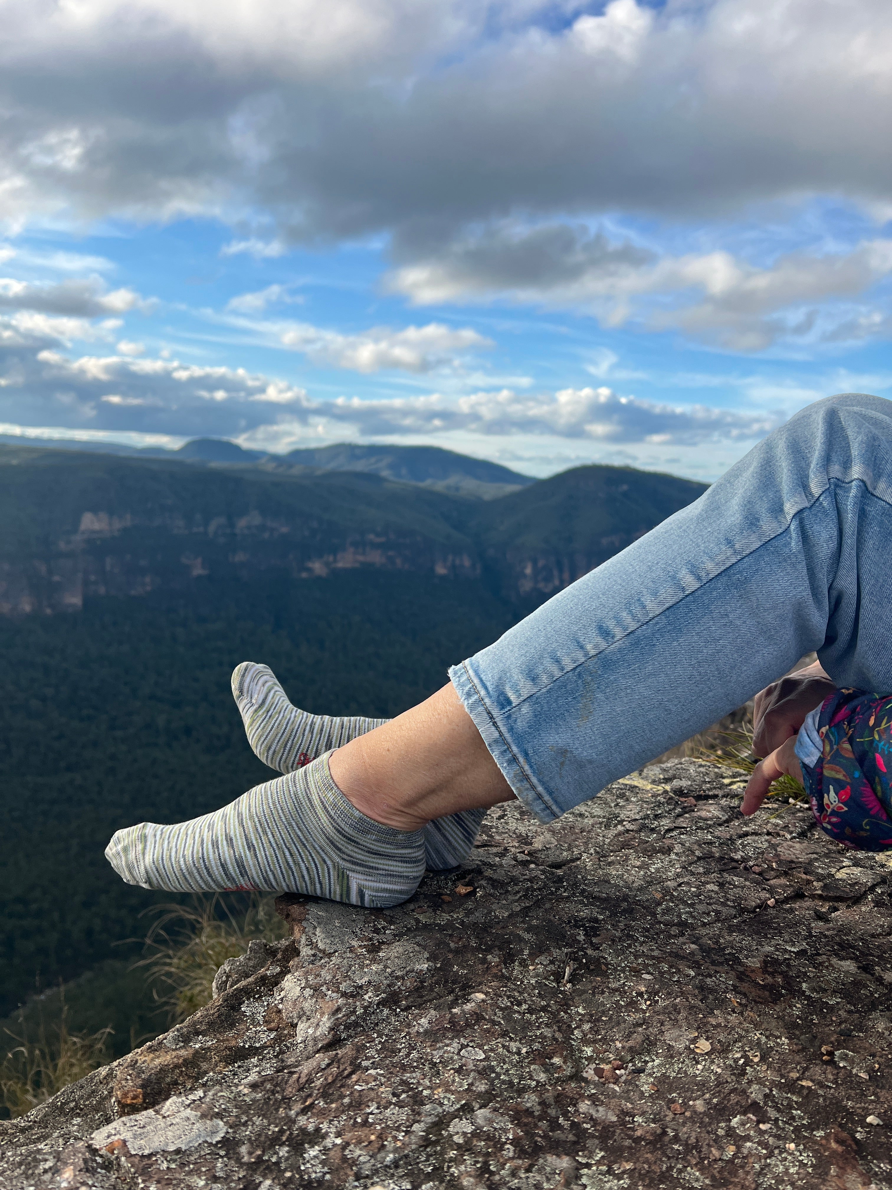 Person sitting on a rock face with a scenic view of clouds and sky.