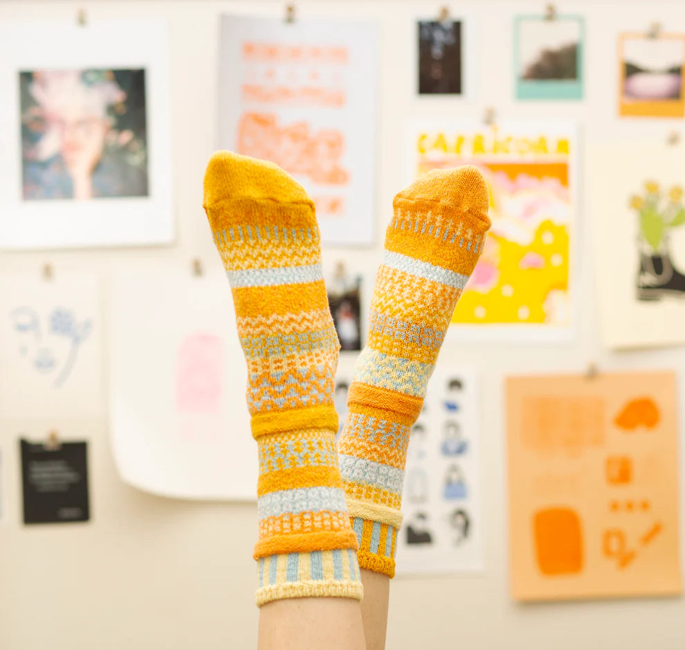 Yellow and orange patterned socks worn indoors with a colorful background