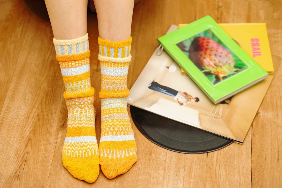 Person wearing yellow patterned socks on a wooden floor with books and a record player.