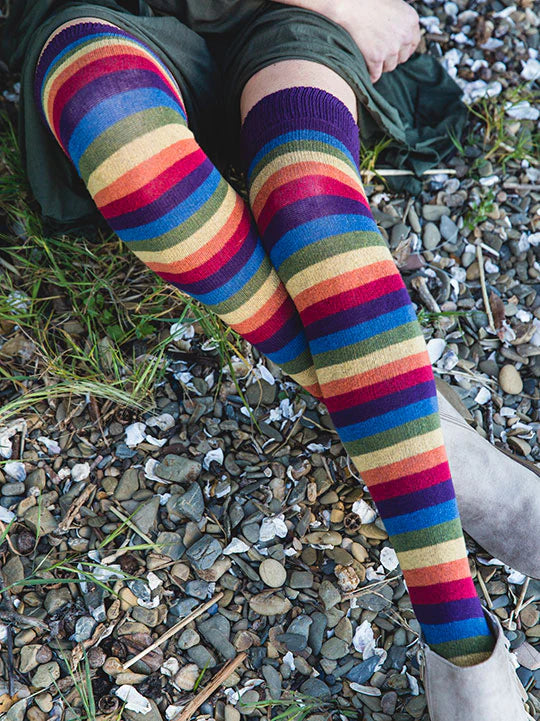 Person wearing colorful striped socks sitting on a rocky ground.