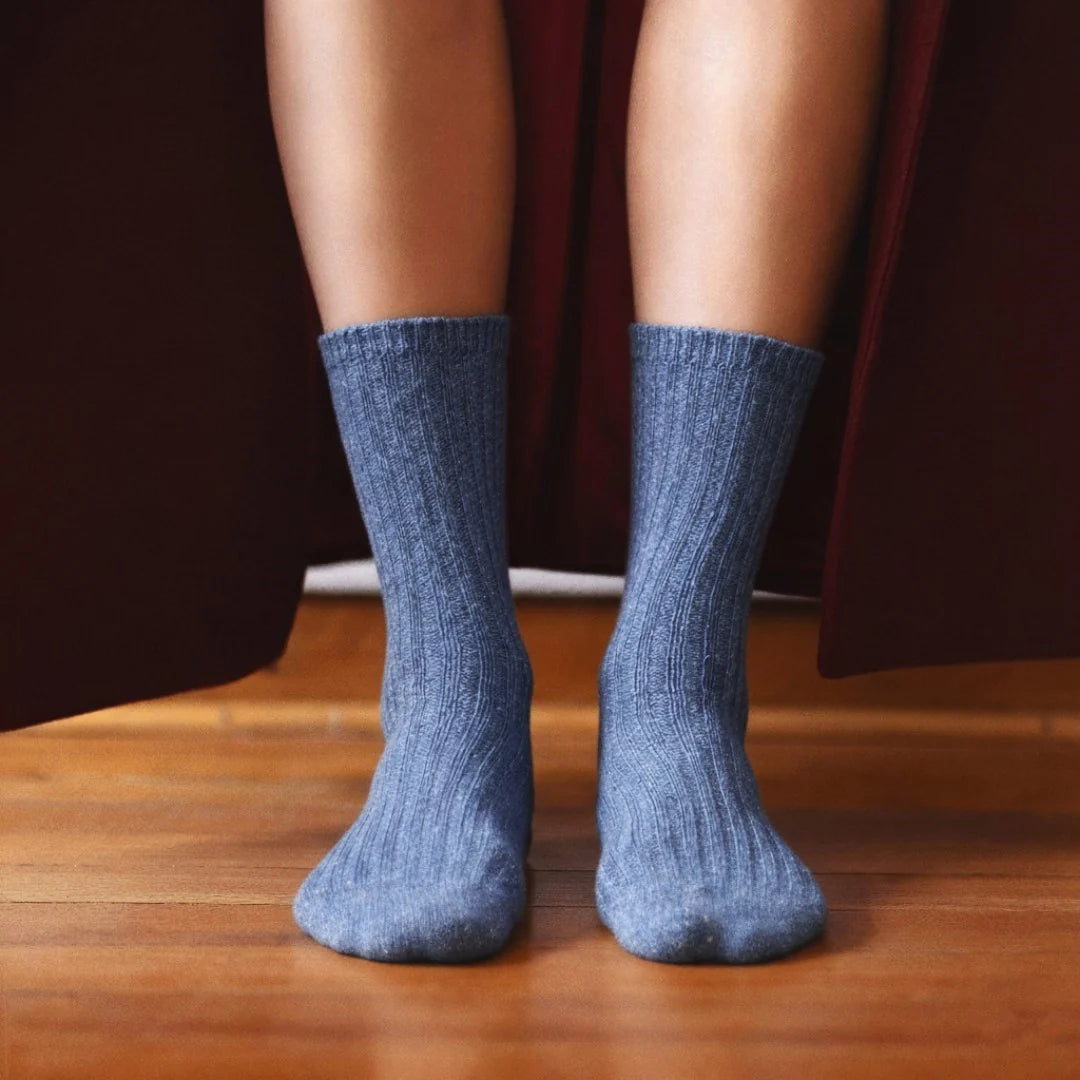 Blue socks worn on feet standing on a wooden floor with a dark curtain background