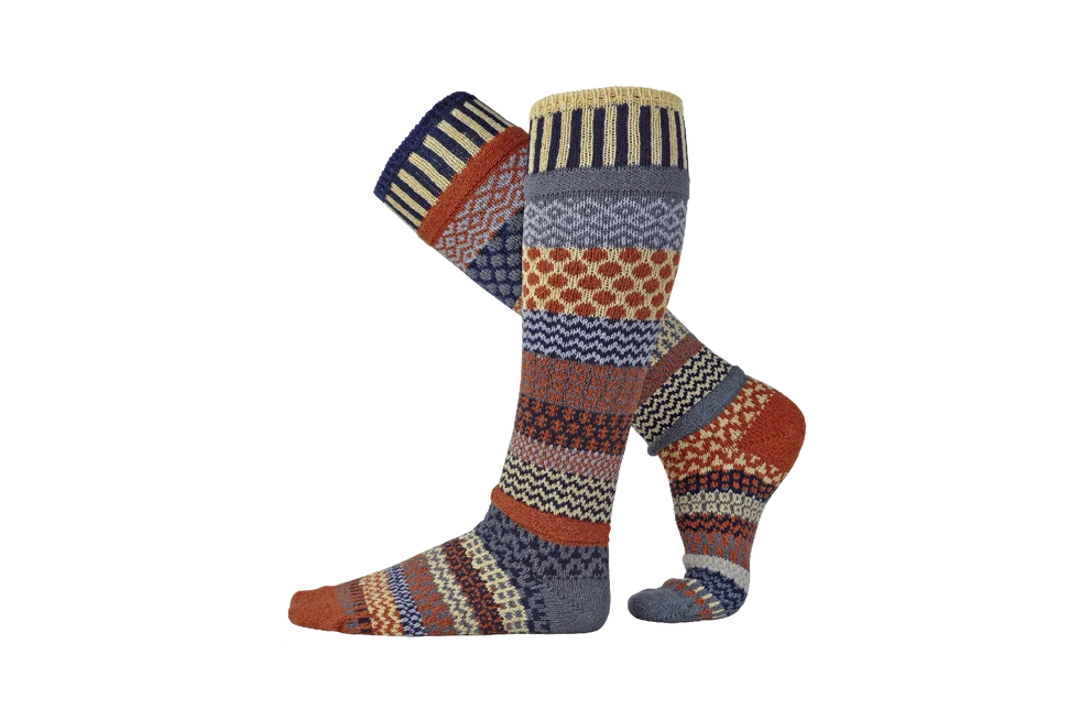A pair of knee-high socks with a multicolor geometric and tribal pattern, featuring shades of orange, blue, red, yellow, and brown on a white background.