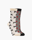 Two crew socks shown on invisible forms against a light gray background. One sock is off-white with black bow patterns and beige heels/toes/cuffs.