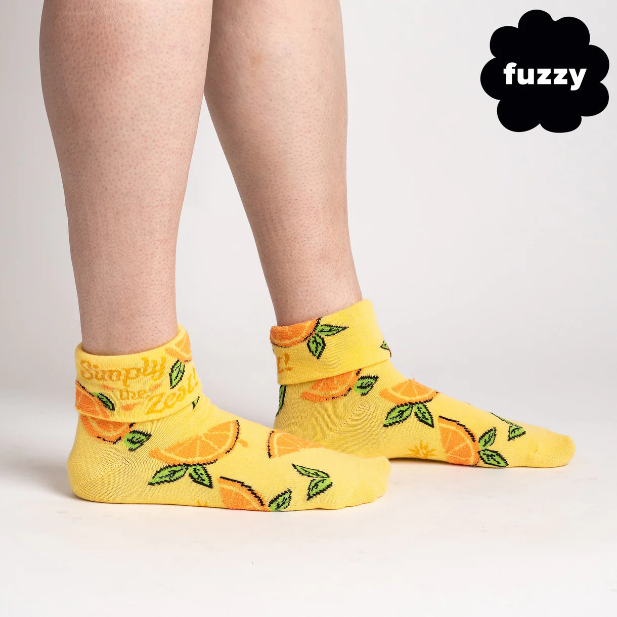 Yellow socks with orange design worn by a person, on a plain background with 'fuzzy' brand logo.