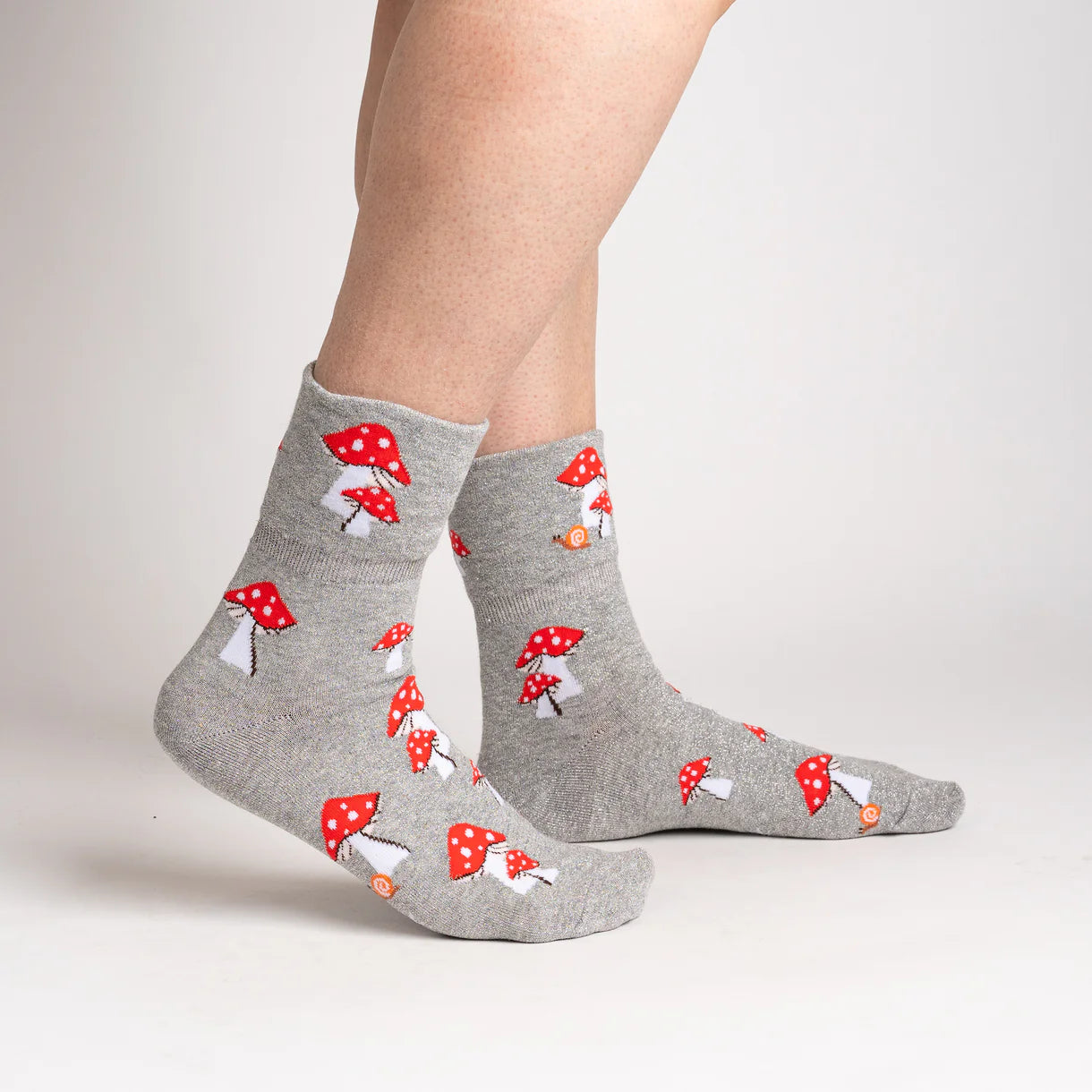 Gray socks with red mushroom pattern worn by a person on a light gray background