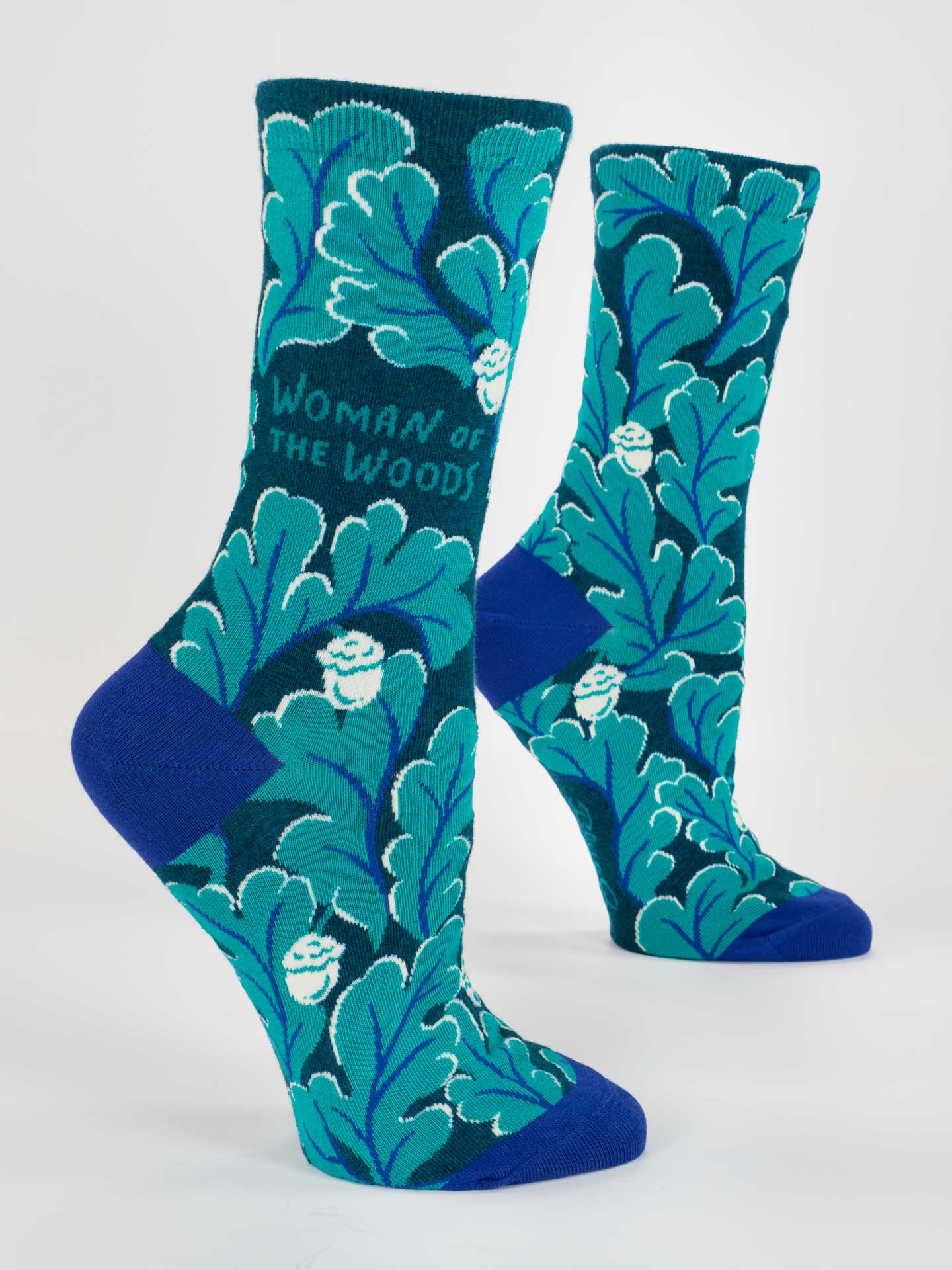 Teal and blue socks with leaf pattern and 'Woman of the Woods' text on a white background