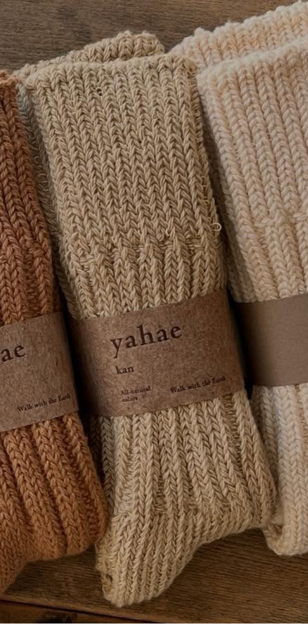 Three pairs of knitted socks with 'yahae' labels on a wooden surface.