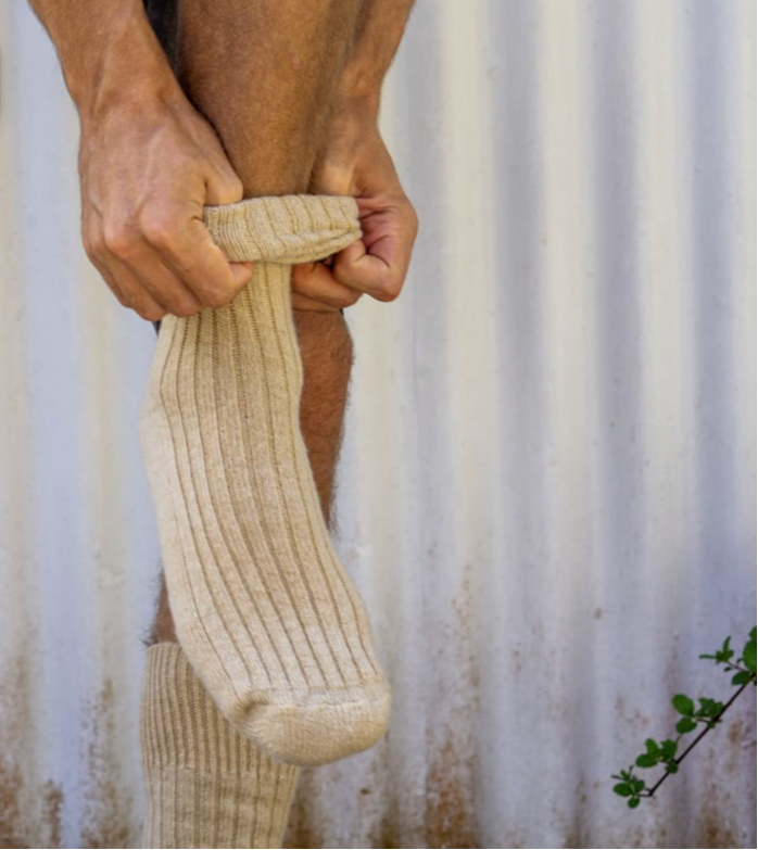 Person wearing a beige sock against a corrugated metal background