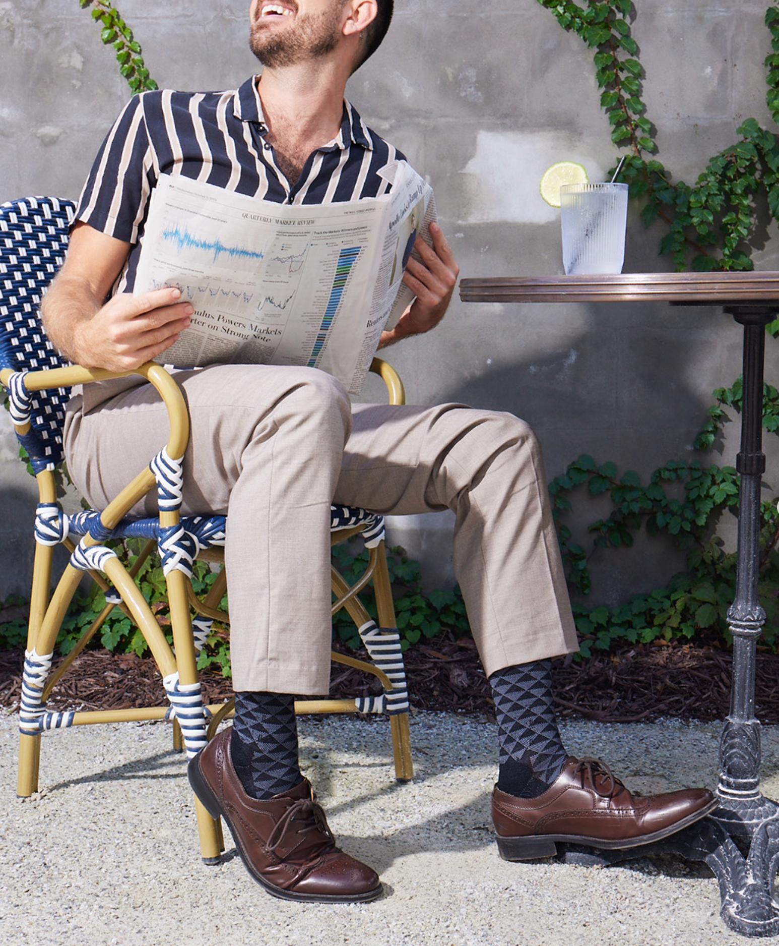 Man sitting outdoors reading a newspaper, wearing striped socks.