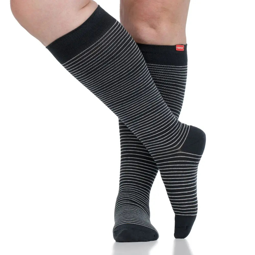 Black and gray striped wide fit compression socks worn by a person on a white background