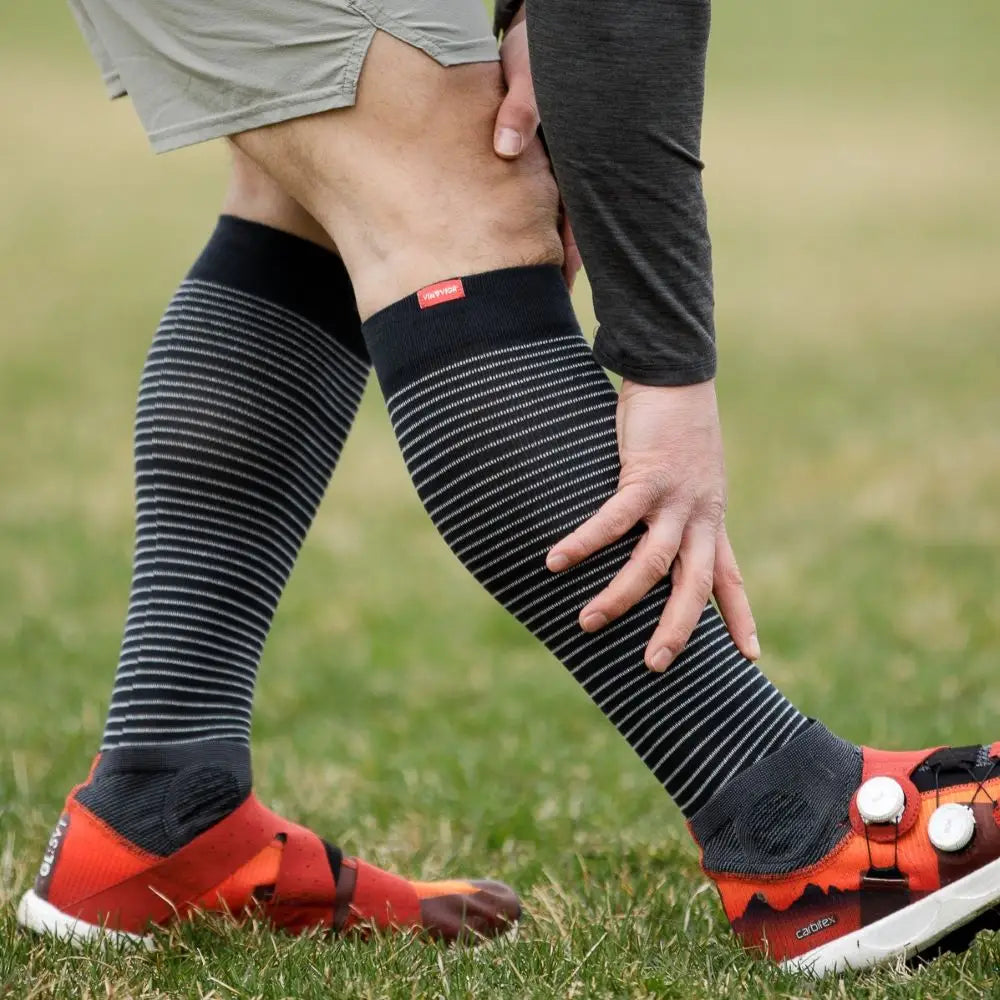 Person wearing black knee-high wide fit compression socks with red accents on grass