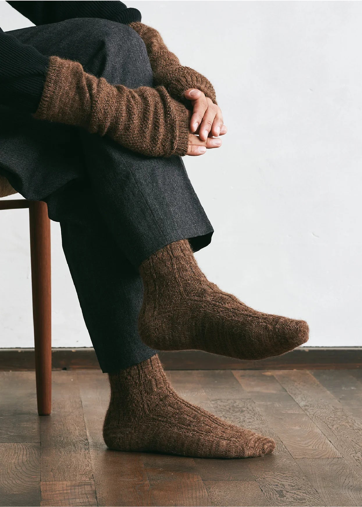 Person wearing brown knitted socks sitting on a wooden chair.