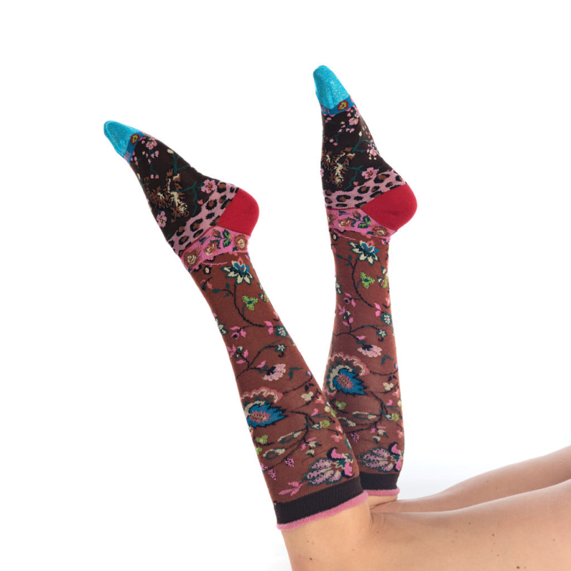 A pair of knee-high socks with a brown floral pattern, pink leopard print cuffs, and bright blue toes, worn on a person's legs against a white background.