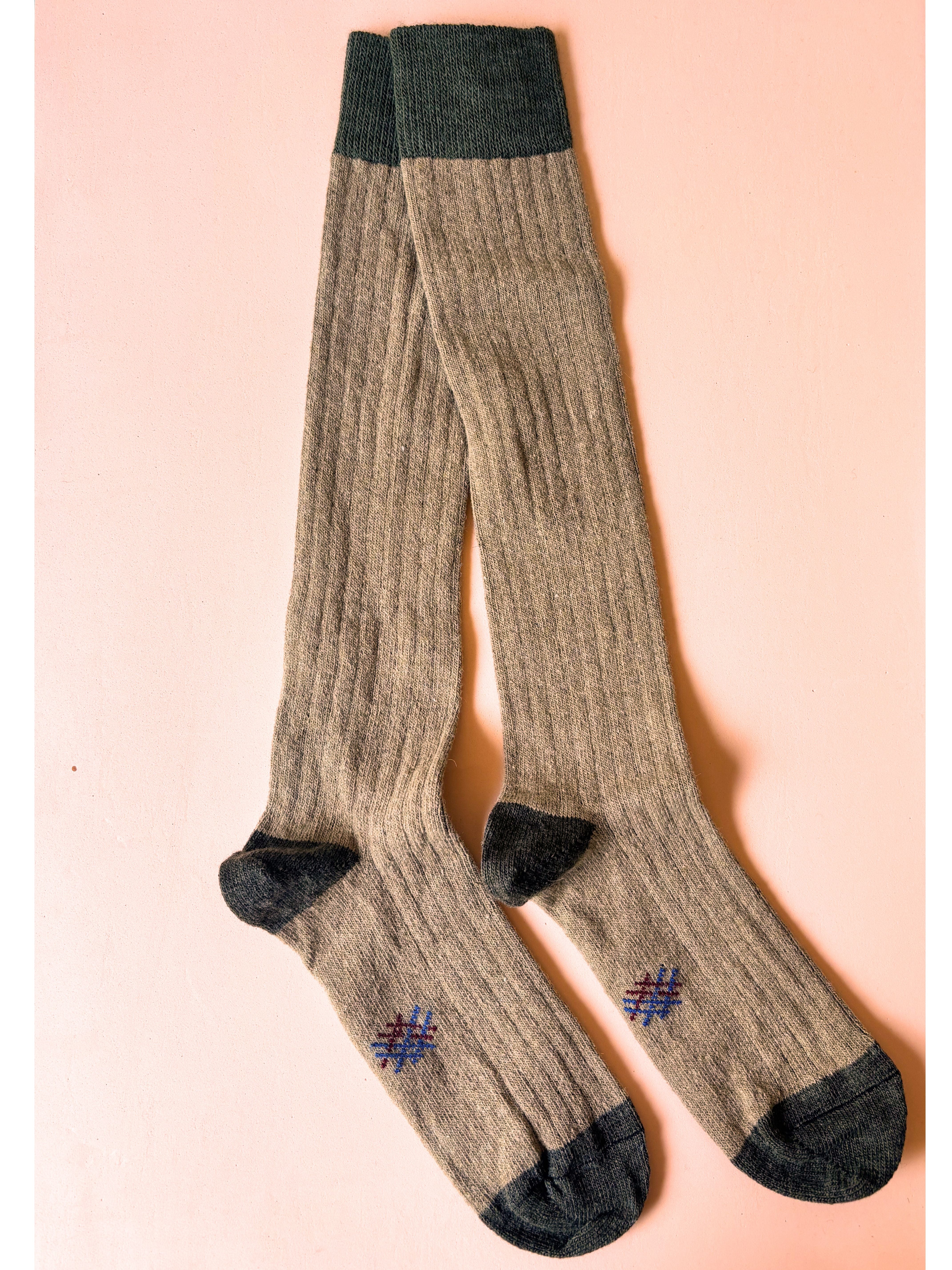 Pair of brown knee-high socks with black toes and cuffs on a pink background