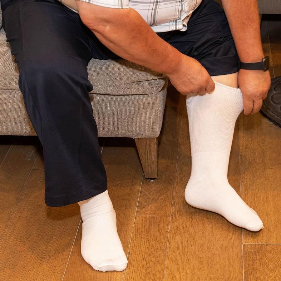 Person sitting on a sofa pulling up a white extra wide athletic sock - The Sockery