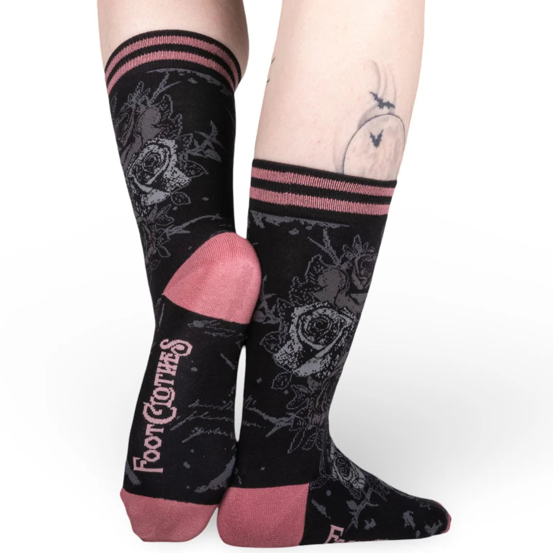 Black socks with floral patterns and pink accents worn by a person on a white background