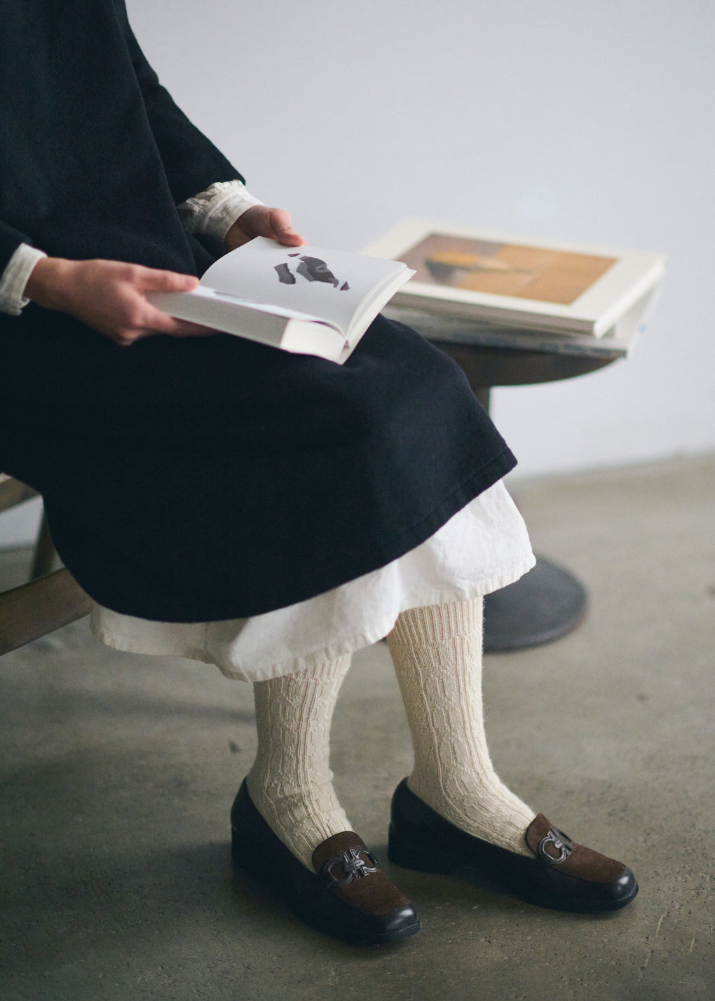 Person sitting on a stool reading a book with natural coloured socks and dark shoes.