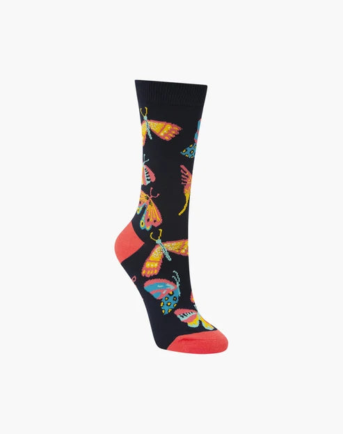 A single crew sock on a white background, featuring a black base with a colorful pattern of butterflies and moths, finished with a bright coral-red toe and heel.