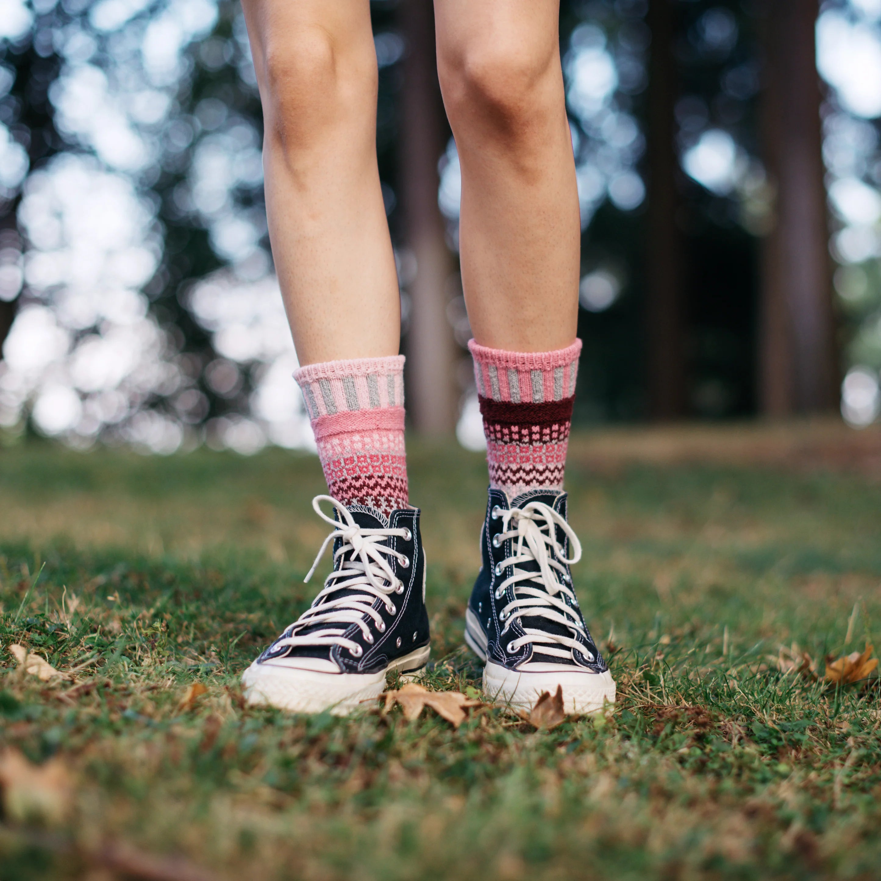 Person wearing pink patterned socks and black high-top sneakers on grass with blurred trees in the background