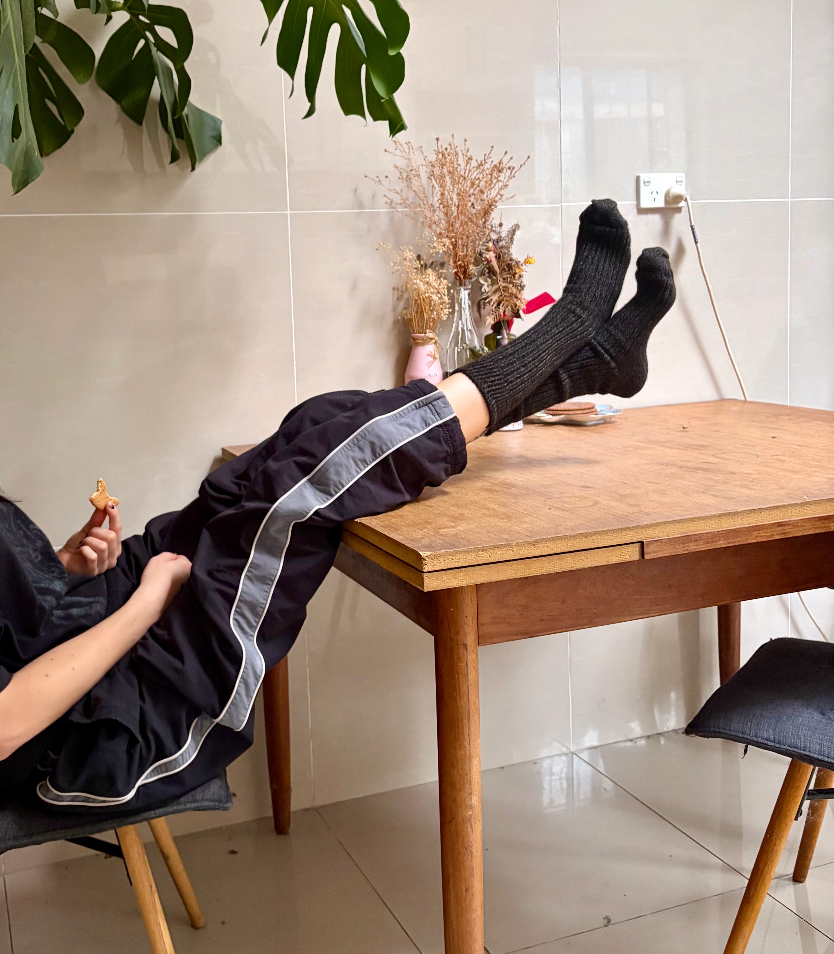 Person wearing black pants with white stripes sitting at a wooden table indoors.