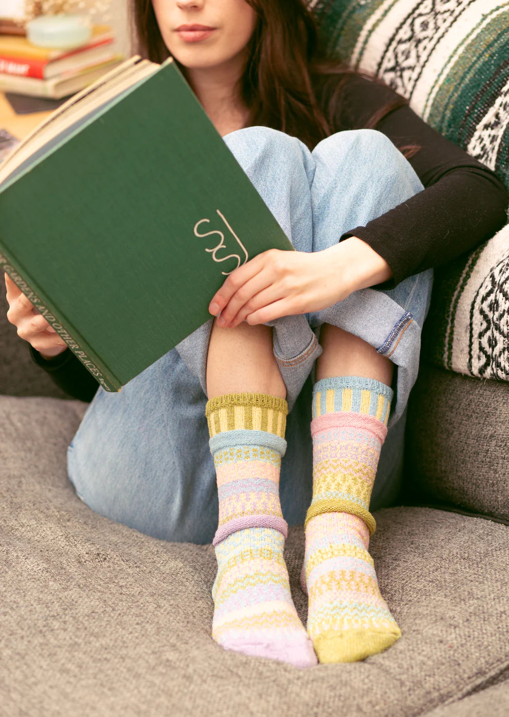 Person sitting on a couch wearing pastel coloured striped socks, holding a green book.