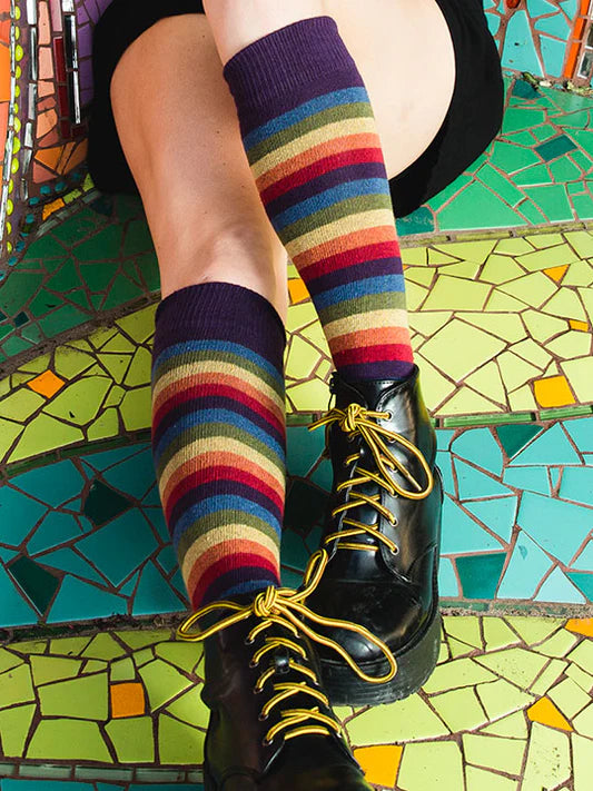 Colourful striped socks worn with black shoes on a mosaic floor.