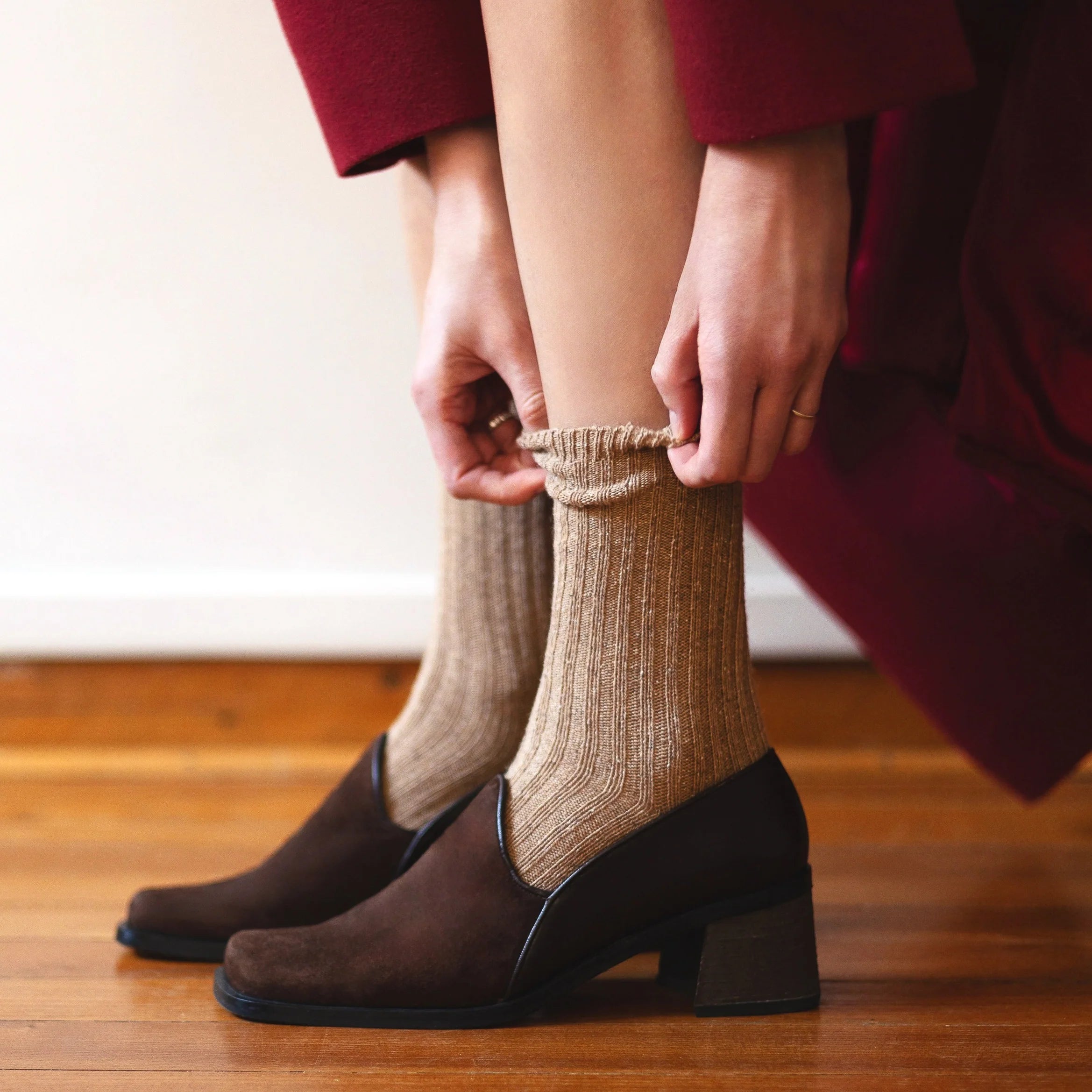 Person wearing brown shoes and beige socks on a wooden floor.
