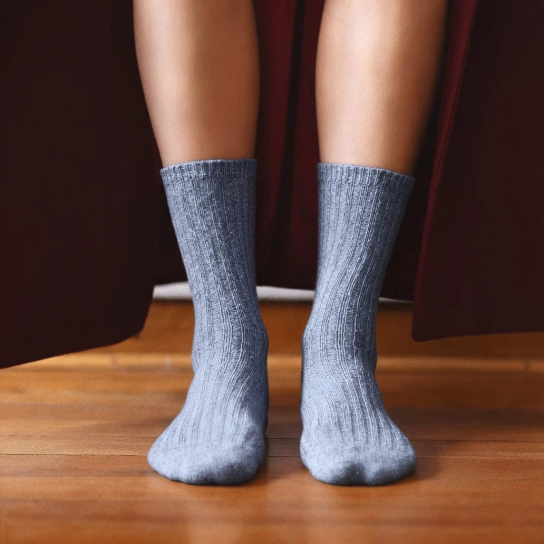 Gray socks worn on a wooden floor with a dark curtain background