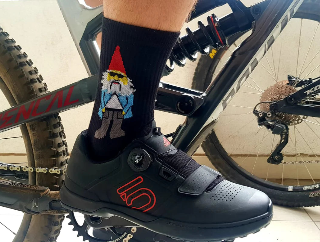 Person wearing black cycling shoes and socks with a gnome design on a bicycle.