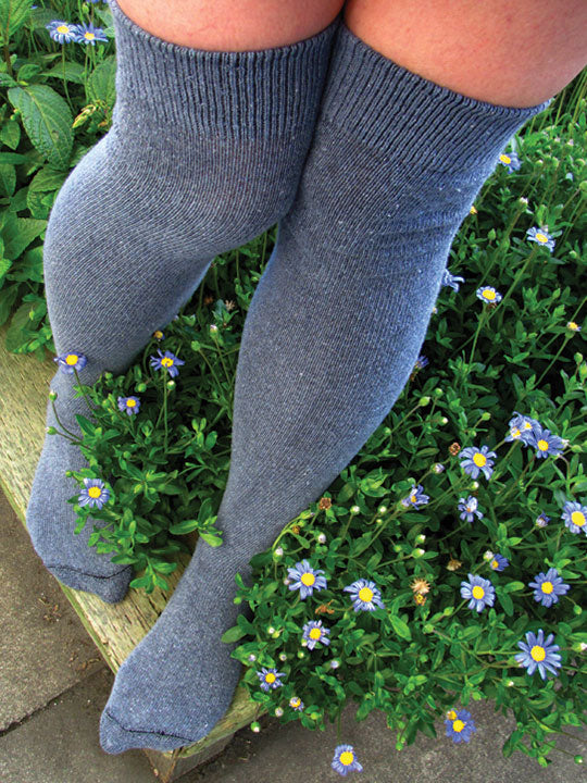 Person wearing gray knee-high socks standing on a stone step with greenery and flowers in the background