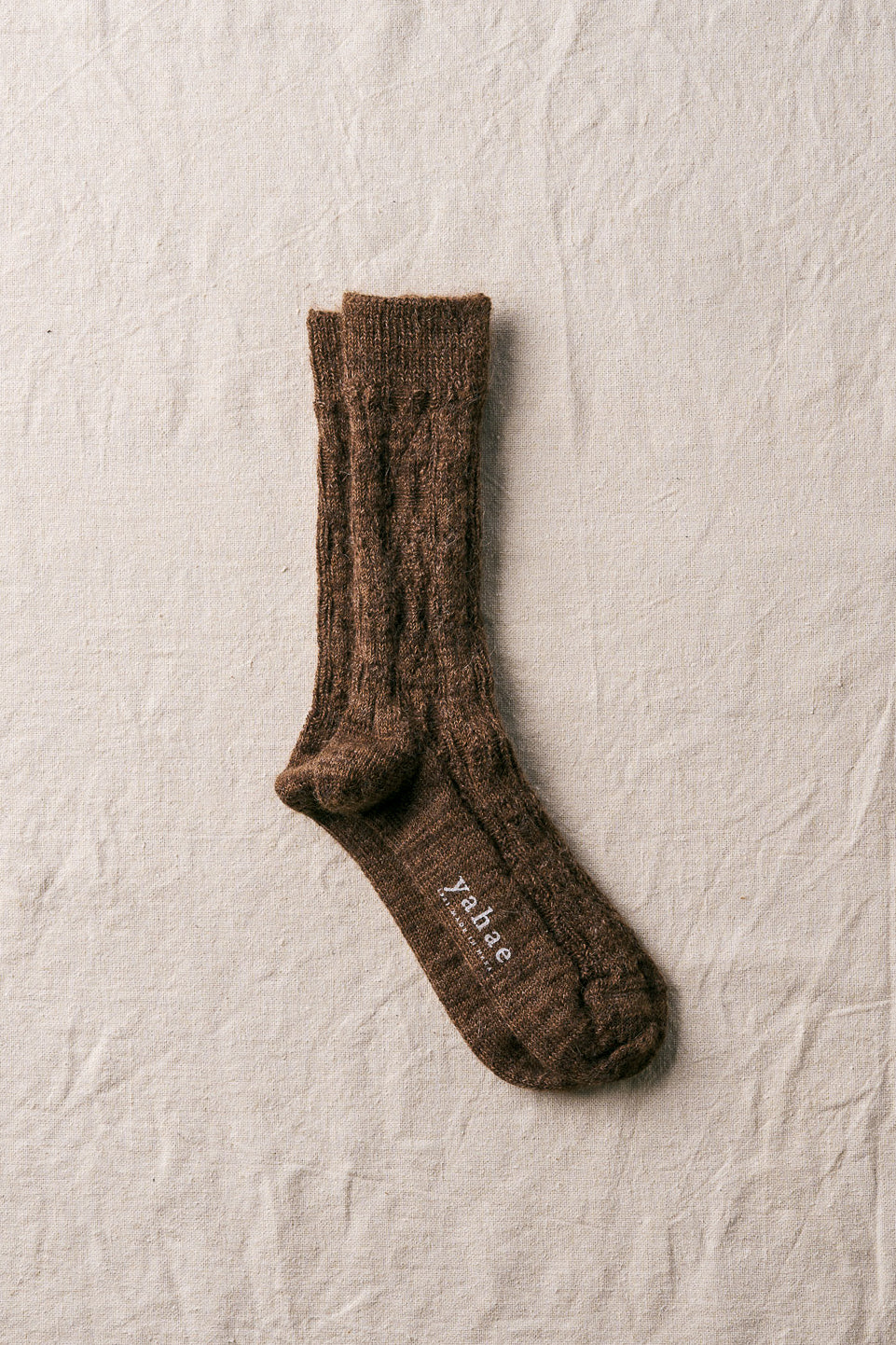 Brown sock with 'Yahae branding on a textured beige background