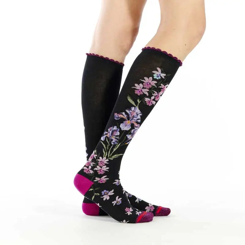 Black knee-high socks with floral patterns worn by a person on a white background