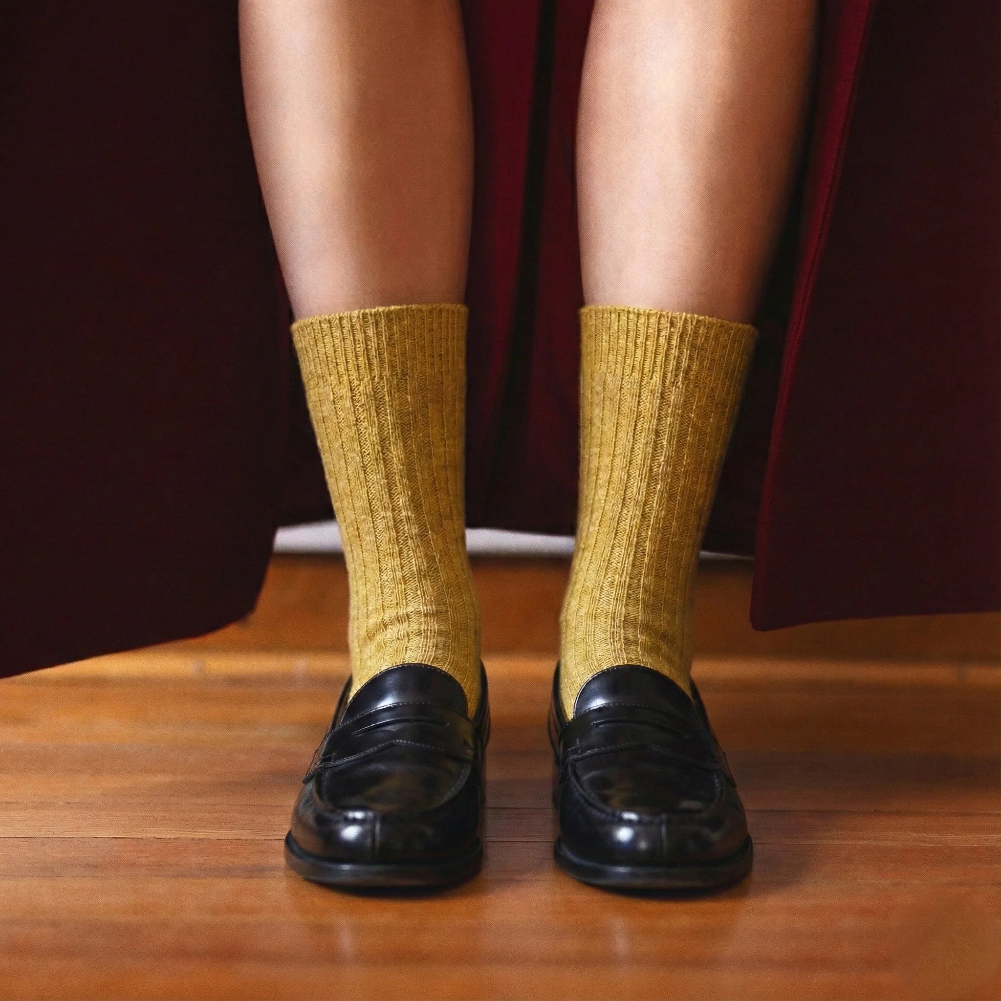 Person wearing mustard yellow socks and black shoes on a wooden floor.