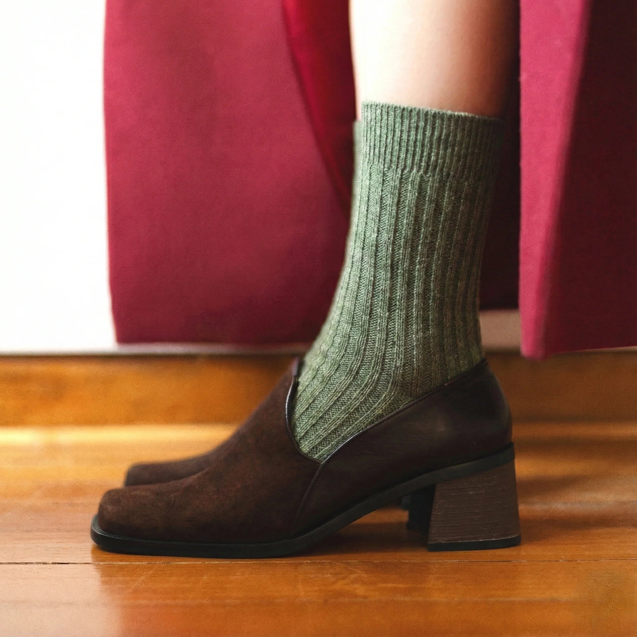 Person wearing green socks and brown shoes on a wooden floor.