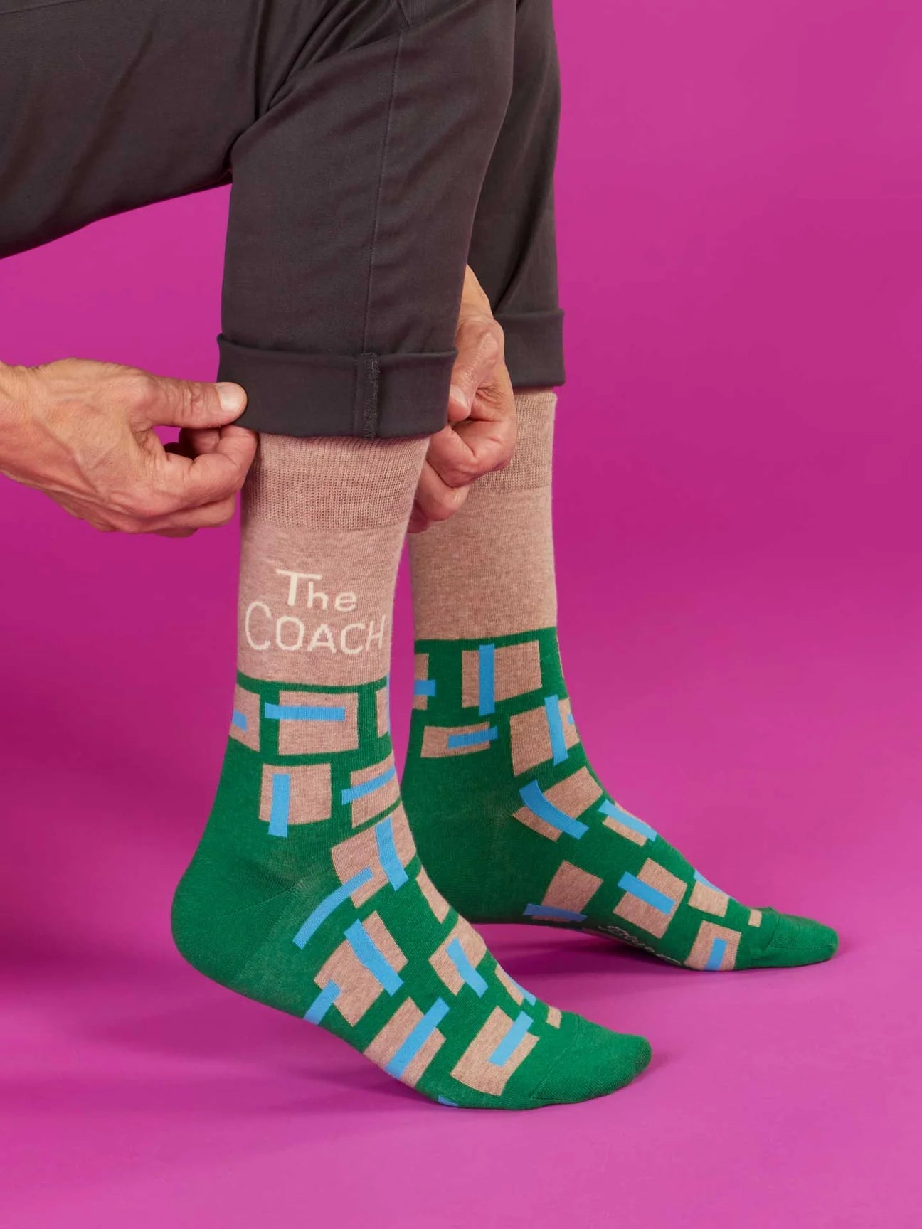 Person wearing green patterned socks with 'The Coach' text on a pink background