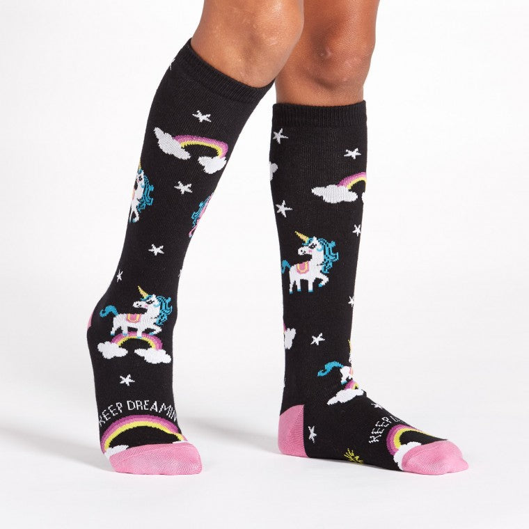 Knee high black socks with rainbows and white unicorns and stars. The words "Keep Dreamin' " are written across the foot - The Sockery