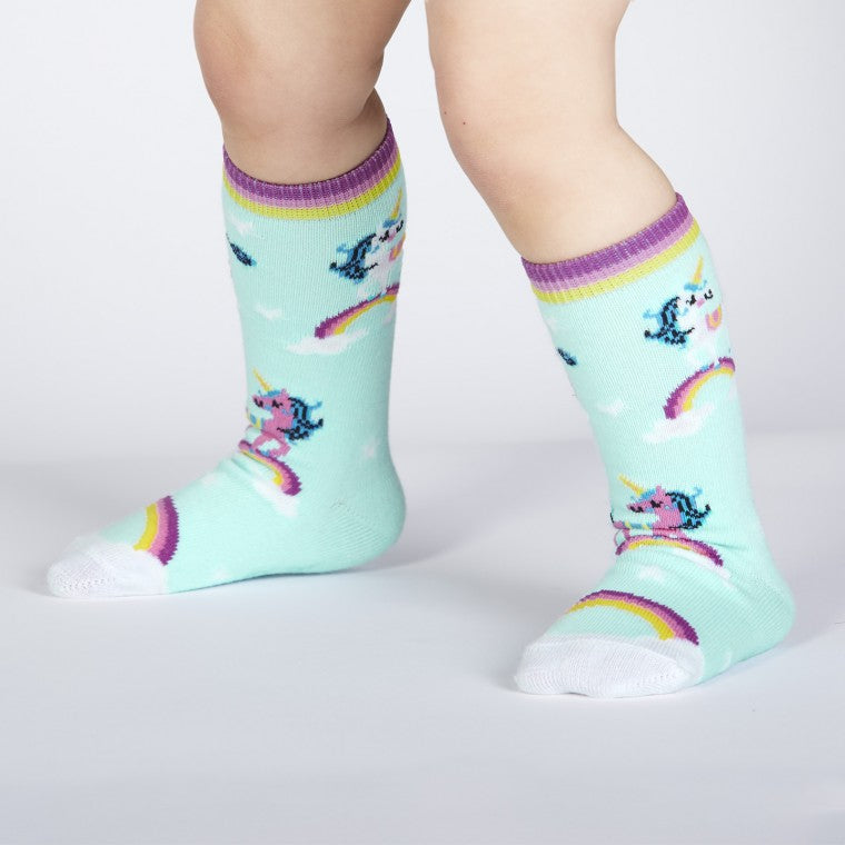 Toddler wearing mint green knee high socks. There are white and pink unicorns standing on rainbows all over - The Sockery