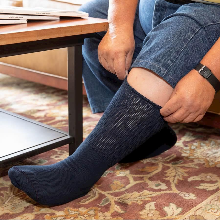 A person sitting on a sofa pulling up an extra wide medical crew sock in black - The Sockery