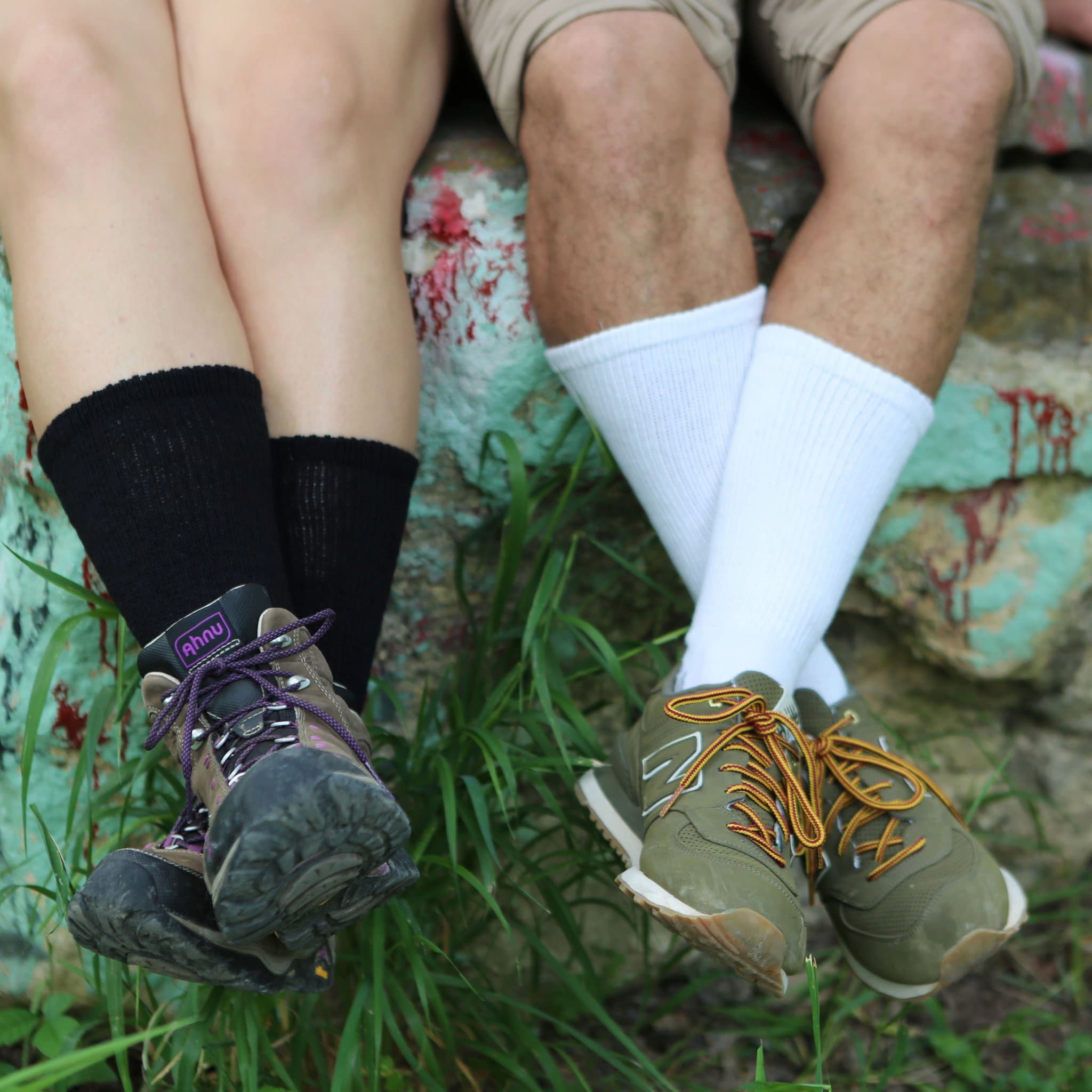 Two people sitting next to each other on a wall. One person is wearing black, the other white loose fit crew socks. They are wearing hiking and sport shoes - The Sockery